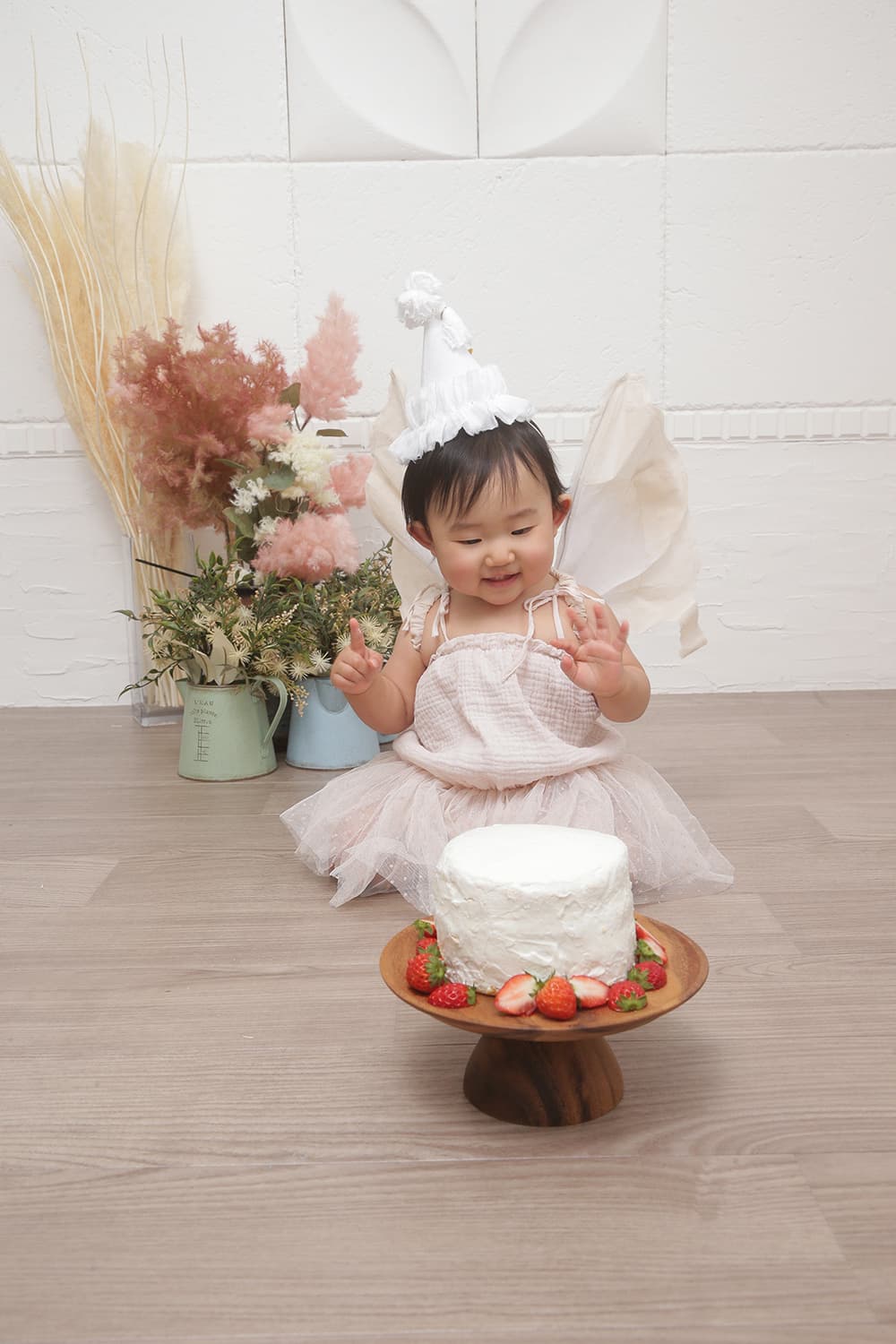 茨城県鉾田市光翔　レンタル＆フォトスタジオ。1歳のお誕生日を迎え白いドレスを着た女の子がケーキの前に座っている画像